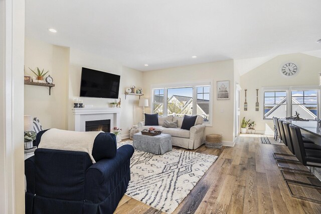 living area with recessed lighting, a warm lit fireplace, baseboards, and wood finished floors