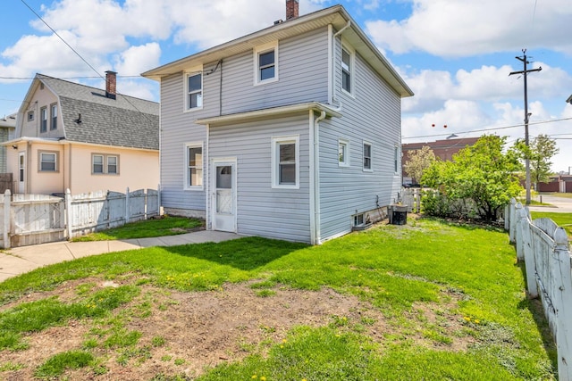 back of property with a chimney, fence, and a lawn