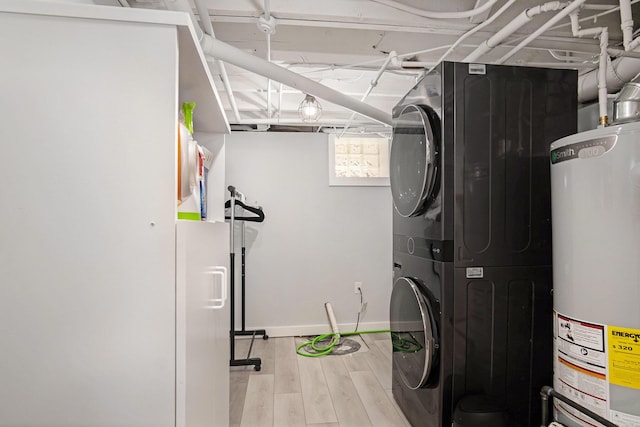 clothes washing area with stacked washer / drying machine, water heater, light wood-style flooring, and baseboards