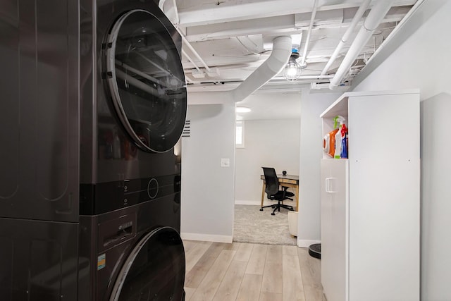 laundry area with stacked washer / drying machine, light wood-style floors, a desk, and baseboards