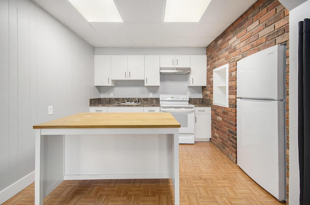 kitchen featuring white appliances, a sink, under cabinet range hood, a paneled ceiling, and brick wall