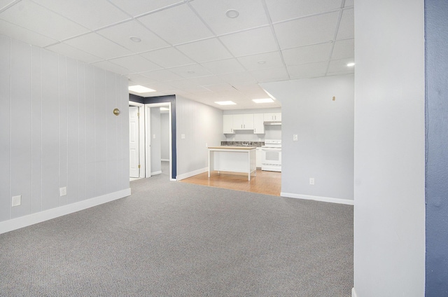 unfurnished living room with light colored carpet, a paneled ceiling, and baseboards