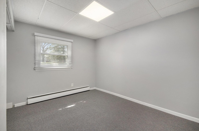 carpeted empty room with a baseboard heating unit, a drop ceiling, and baseboards