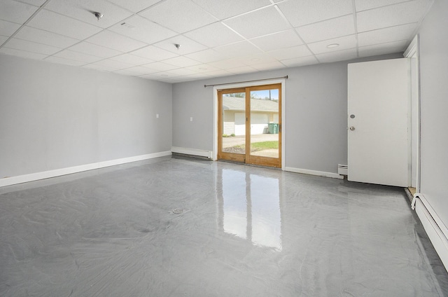 empty room featuring a baseboard heating unit, a paneled ceiling, concrete flooring, and baseboards