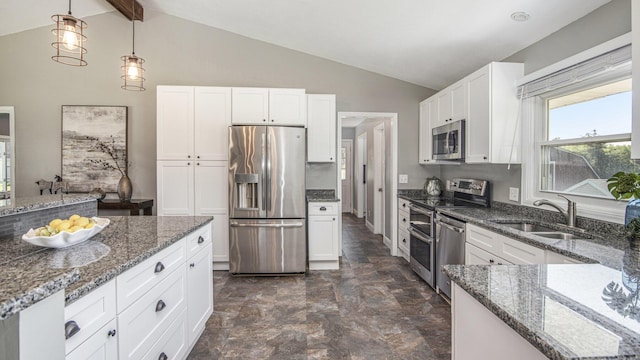 kitchen featuring appliances with stainless steel finishes, a sink, dark stone counters, white cabinets, and hanging light fixtures