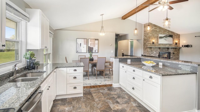 kitchen featuring a sink, dishwasher, a brick fireplace, a peninsula, and white cabinets