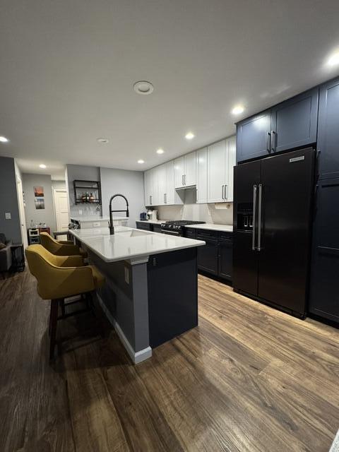 kitchen featuring black appliances, wood finished floors, light countertops, a center island with sink, and a kitchen breakfast bar