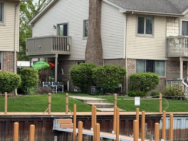 back of house with brick siding, a balcony, and a shingled roof