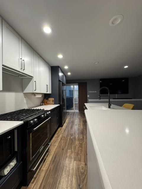 kitchen featuring black appliances, dark wood finished floors, a sink, light countertops, and recessed lighting