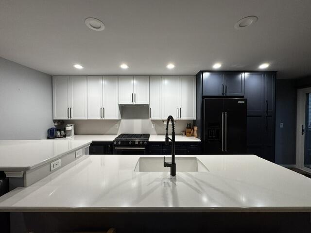 kitchen featuring black appliances, a sink, light countertops, recessed lighting, and white cabinetry