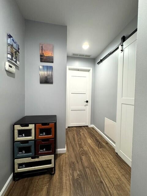 corridor featuring a barn door, wood finished floors, and baseboards