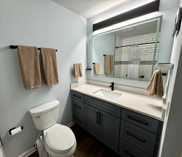bathroom with tiled shower, baseboards, toilet, wood finished floors, and vanity