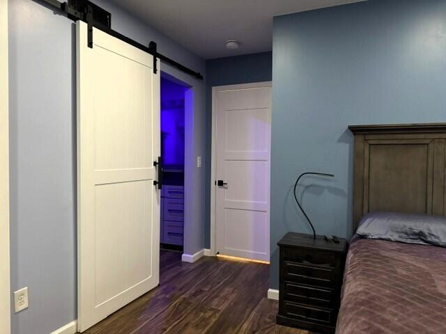 bedroom with a barn door, dark wood-style flooring, and baseboards