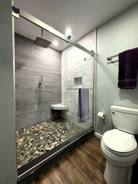 full bath featuring toilet, a shower stall, wood finished floors, and baseboards