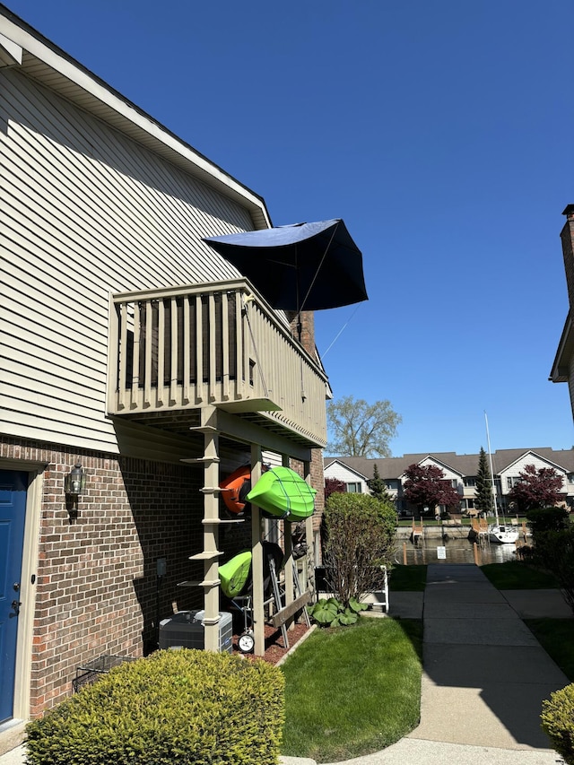 view of side of property featuring a balcony, brick siding, and central AC unit