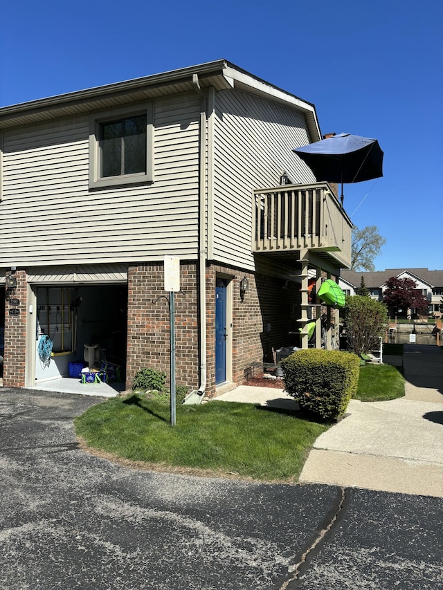 view of side of property with an attached garage, a balcony, brick siding, and asphalt driveway