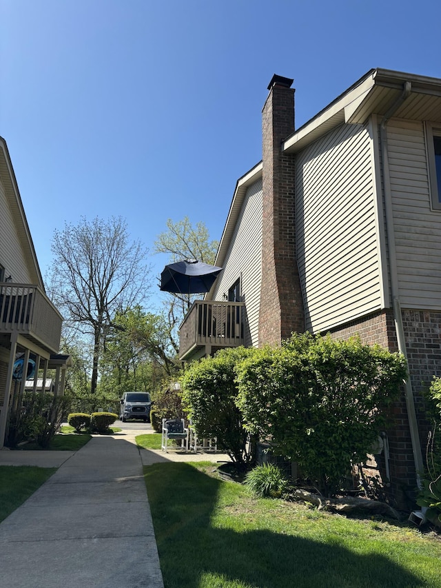 view of property exterior with a chimney, a yard, brick siding, and a balcony