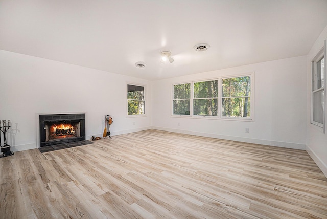 unfurnished living room featuring light wood-type flooring, baseboards, visible vents, and a fireplace with flush hearth