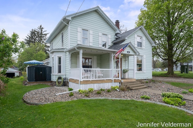 victorian house with a porch, a storage shed, a front yard, a chimney, and an outdoor structure