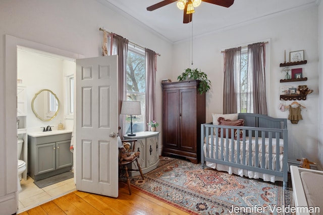 bedroom featuring multiple windows, ornamental molding, light wood-type flooring, a sink, and ensuite bathroom