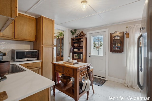 kitchen featuring appliances with stainless steel finishes, light countertops, light tile patterned floors, brown cabinets, and baseboards