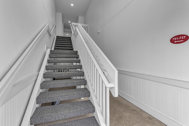 stairway with a decorative wall, a wainscoted wall, and recessed lighting