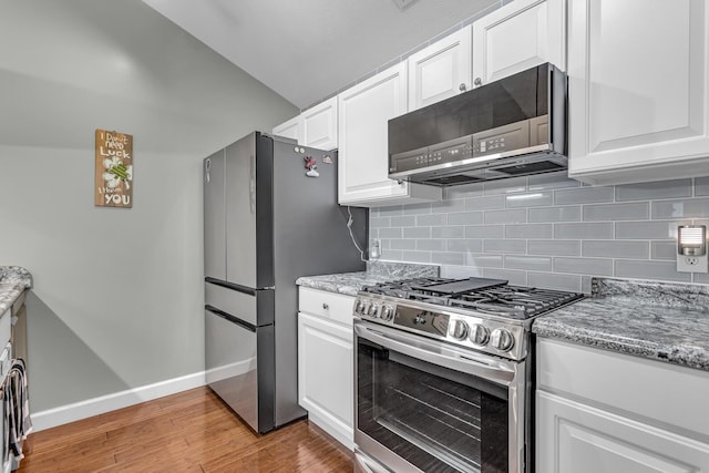 kitchen with stainless steel appliances, backsplash, baseboards, lofted ceiling, and white cabinets