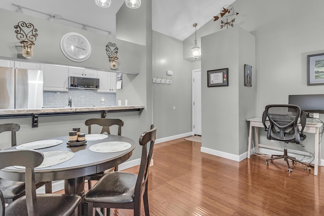 dining space with track lighting, high vaulted ceiling, light wood finished floors, baseboards, and an office area