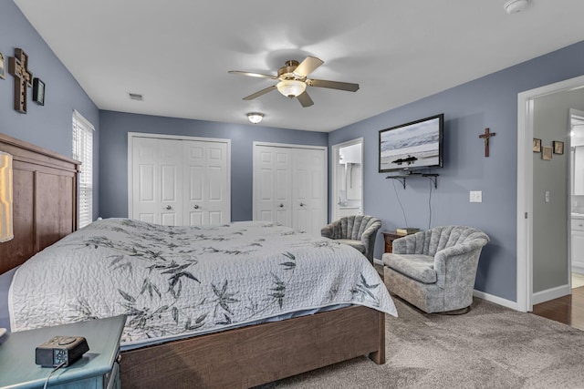 bedroom featuring multiple closets, baseboards, ensuite bath, carpet, and a ceiling fan