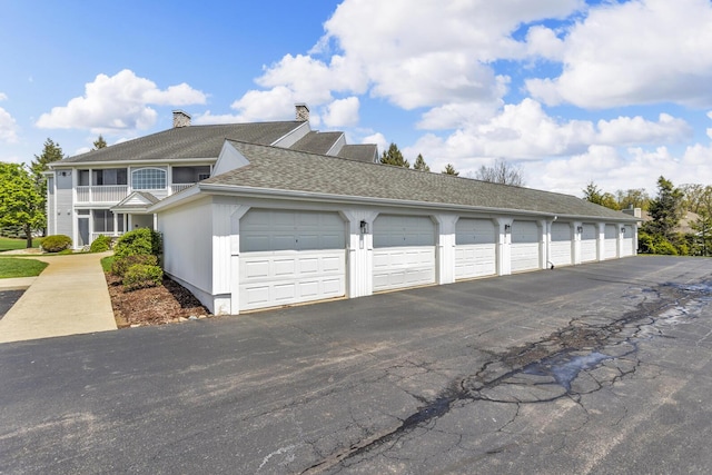 view of property exterior featuring community garages, a chimney, and roof with shingles