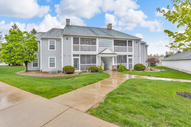 view of front of home with a sunroom, a chimney, a front yard, and a shingled roof