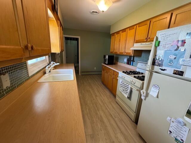 kitchen with white appliances, a sink, decorative backsplash, under cabinet range hood, and brown cabinets