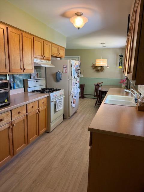 kitchen featuring white gas stove, a sink, under cabinet range hood, brown cabinets, and light wood finished floors