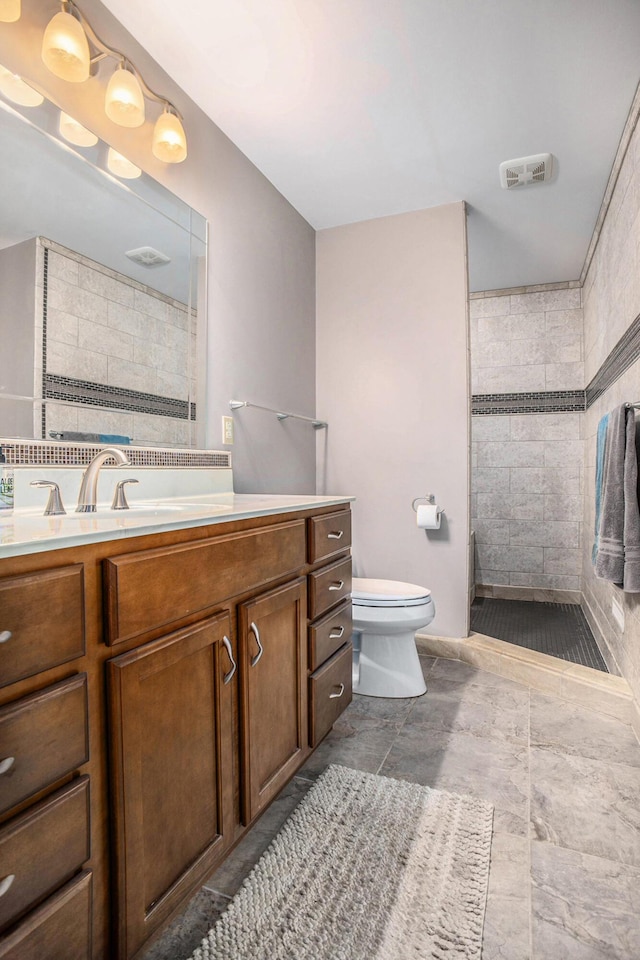 full bathroom featuring tiled shower, toilet, vanity, and tile walls