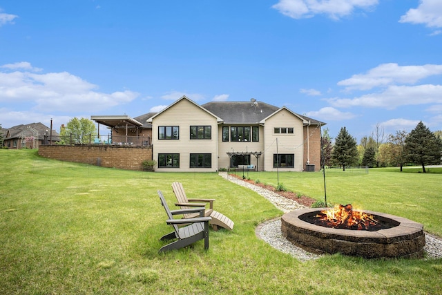 back of property with a fire pit and a lawn