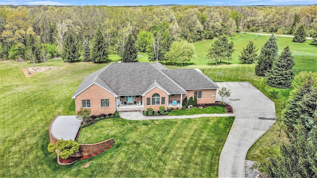view of front of home featuring a porch, a forest view, brick siding, and a front yard