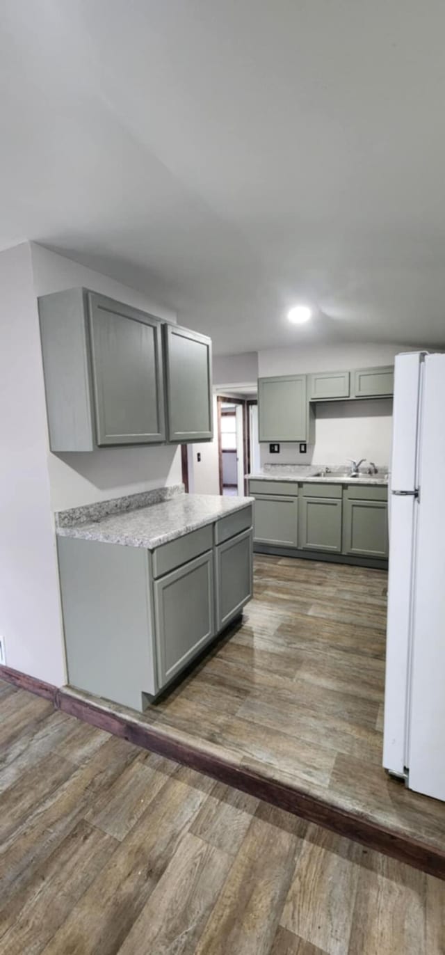 kitchen featuring freestanding refrigerator, gray cabinets, wood finished floors, a sink, and light countertops
