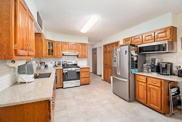 23127 Kendaville Rd, Pierson, MI 49339 - kitchen with appliances with stainless steel finishes, under cabinet range hood, decorative backsplash, and brown cabinetry