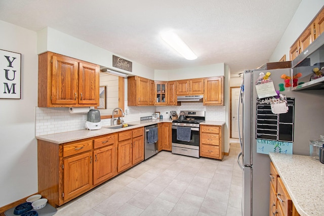 23127 Kendaville Rd, Pierson, MI 49339 - kitchen featuring stainless steel appliances, a sink, under cabinet range hood, backsplash, and brown cabinets