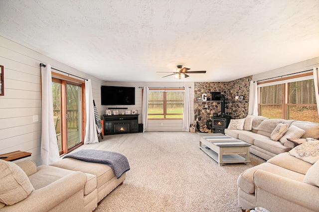 23127 Kendaville Rd, Pierson, MI 49339 - living room featuring a wood stove, healthy amount of natural light, a textured ceiling, light carpet, and a ceiling fan