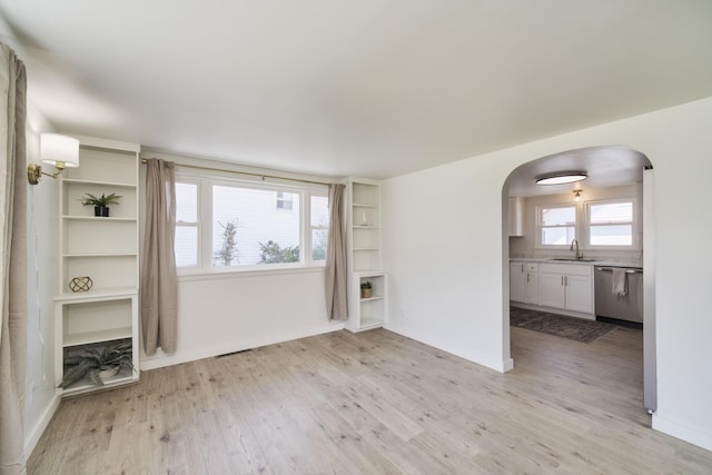 923 Maple St, Ludington, MI 49431 - unfurnished living room featuring arched walkways, light wood-type flooring, a sink, and baseboards
