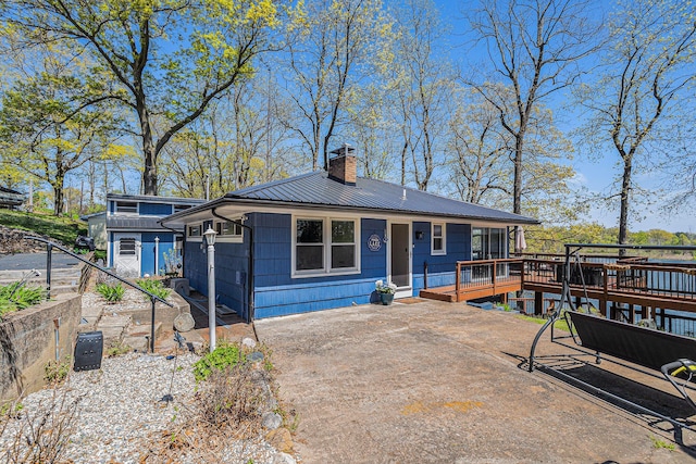 view of front facade featuring a chimney, a deck, metal roof, and a patio