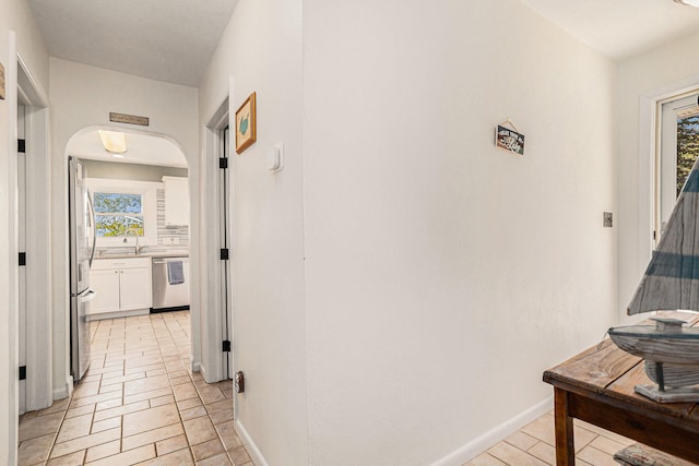 corridor featuring healthy amount of natural light, arched walkways, baseboards, and light tile patterned flooring
