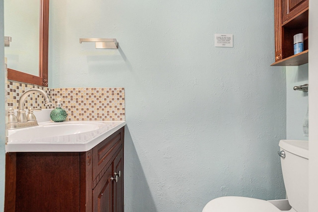 half bath with toilet, vanity, and tasteful backsplash