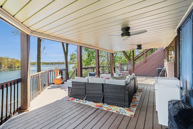 wooden deck with a water view, outdoor lounge area, and ceiling fan