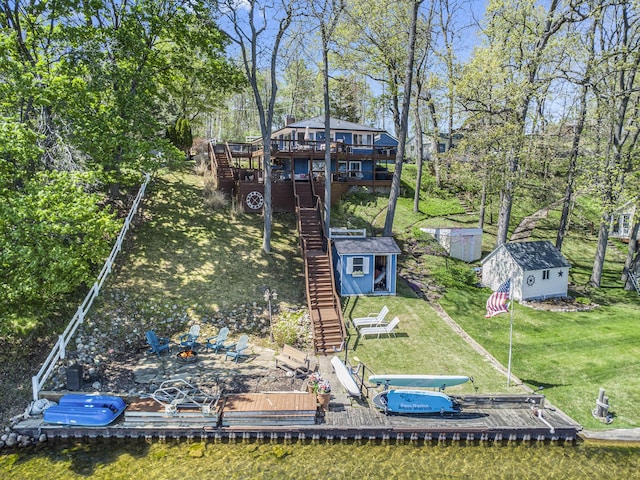 dock featuring stairway, a fire pit, a wooden deck, a lawn, and view of wooded area