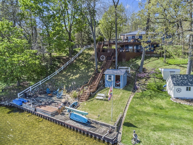 view of green lawn with stairs, a shed, a floating dock, an outbuilding, and a wooden deck
