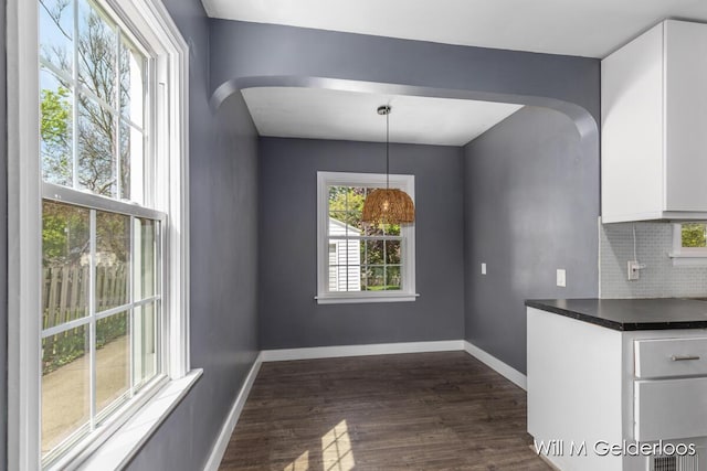 unfurnished dining area featuring arched walkways, dark wood finished floors, and baseboards