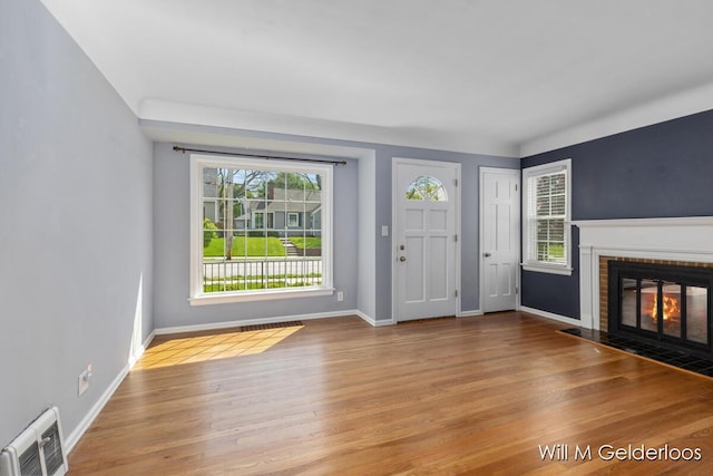 entrance foyer with wood finished floors, a brick fireplace, and baseboards