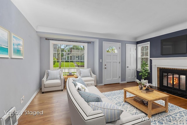 living room with a brick fireplace, light wood-style floors, and baseboards